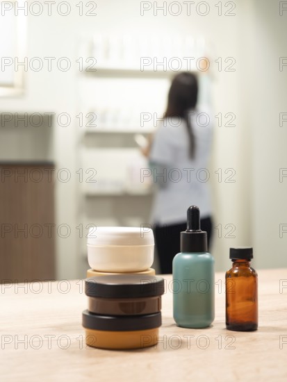 Skincare jars and serum bottles on a wooden table with an aesthetician arranging products in a blurred background