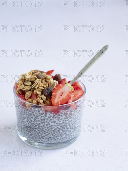 Chia seed pudding in a glass with fresh strawberries, granola, and a spoon, representing healthy breakfast