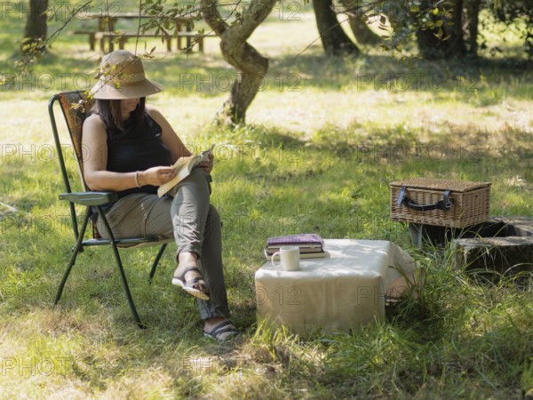 Woman enjoying a peaceful afternoon reading a book in a folding chair under a tree