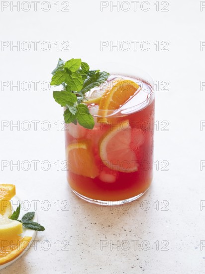 Glass of cold fruit juice with orange, lemon, and mint on a white background