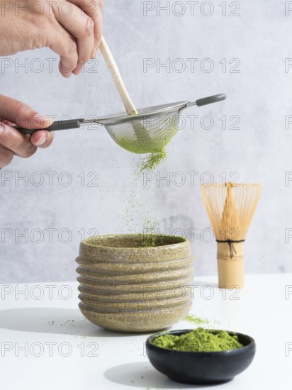 Hand sifting matcha powder through a sieve into a ceramic tea bowl during preparation