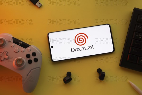 Dhaka, Bangladesh- 23 March 2025: Dreamcast logo displayed on a smartphone surrounded by gaming accessories in an yellow light