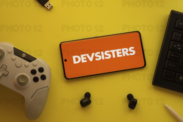 Dhaka, Bangladesh- 23 March 2025: Devsisters logo displayed on a smartphone surrounded by gaming accessories in an yellow light