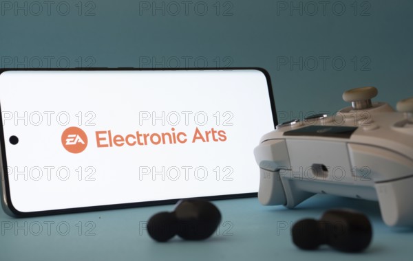 Dhaka, Bangladesh- 23 Mar 2025: A smartphone with a Electronic Arts icon next to a controller and earbuds on a blue surface