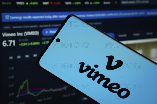 Dhaka, Bangladesh- 17 March 2025: Vimeo logo is displayed on a smartphone screen, with a stock graph webpage visible on a computer screen in the background