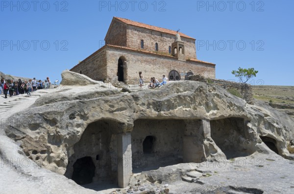 Historic church on a rock with caves and tourists on a clear day, 10th century princely church, Uplistsikhe cave town, Uplistsikhe, Inner Kartli region, Shida Kartli, Georgia