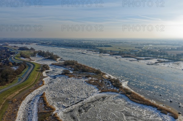 On a cold winter day, a barge sails upstream on the Elbe near Hamburg with slight ice. The foothills of the Elbe are icy in the flooded area. On the left, the Elbufer-Straße Kraueler Hauptdeich and the Hamburger Vier- und Marschlande. Lower Saxony in the background. Kirchwerder, Hamburg, Germany