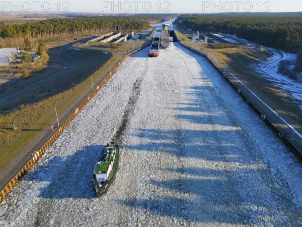 A ship sails through a long, icy waterway lined with locks in a wide landscape, aerial view, icebreaker sea bear from Magdeburg and cargo ship Cologne 2 and Cologne 1, Hohenwarthe lock, Elbe-Havel Canal, Jerichower Land, Saxony-Anhalt, Germany