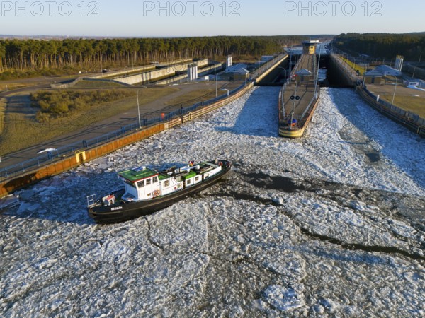 A ship navigates through an ice-covered channel in front of a lock in a wintry landscape with forest in the background, aerial view, icebreaker sea bear from Magdeburg, Hohenwarthe lock, Elbe-Havel Canal, Jerichower Land, Saxony-Anhalt, Germany