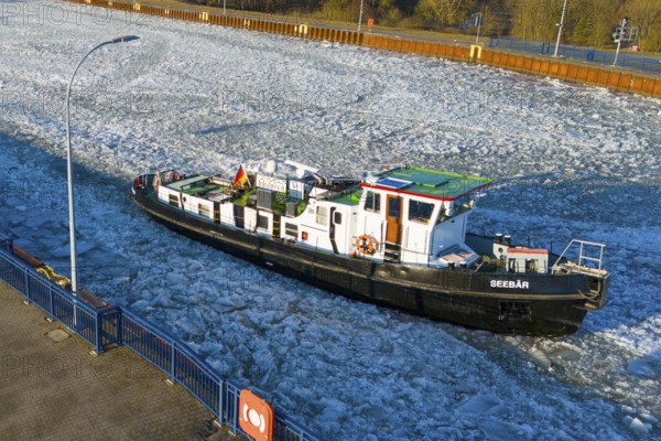 A ship navigates through an ice-covered channel in the harbor area in cold winter weather, aerial view, ice floes, icebreaker sea bear from Magdeburg keeps waterways clear, Elbe-Havel Canal, Jerichower Land, Saxony-Anhalt, Germany