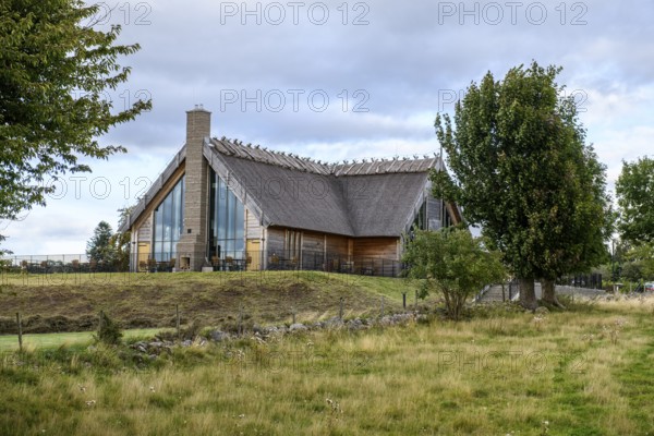 Naturum and Café Doppingen, Naturum Hornborgasjön modern thatched building with glass front and reed roof, which stands in Lake Hornborgasjön and can be reached via footbridges, surrounded by plants under a dramatic sky, Broddetorp, Västra Götalands län, Sweden