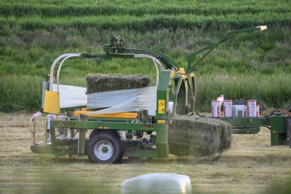 Tractor wraps hay bales in a field with a round baler in plastic film to preserve hay, Osnabrücker Land, Lower Saxony, Germany