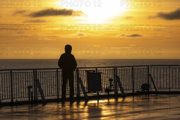 Traveler standing at the railing and looking at the sea at sunset, Finland ferry Helsinki to Travemünde, Baltic Sea
