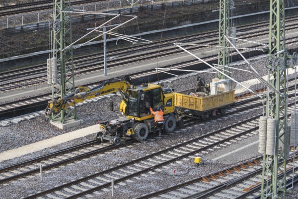 A construction site scene with yellow excavator and wagon near railroad tracks, Untertürkheim parking lot, Stuttgart, Baden-Württemberg, Germany