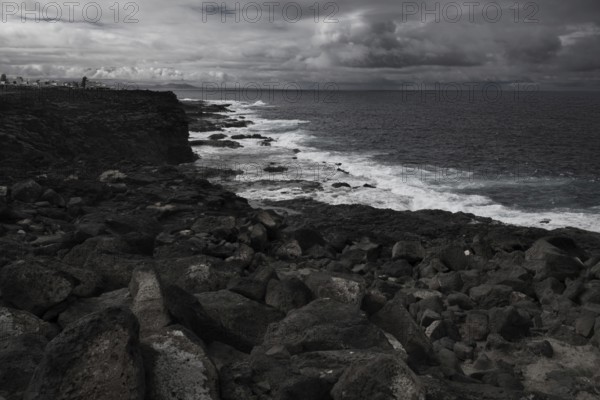 Dramatic, cloudy coastal scene with rough rocks and a wavy sea. Dark, stormy atmosphere, Yaiza Lanzarote