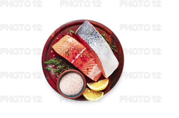 A wooden plate holds two salmon fillets next to lemon slices and a small bowl of salt. Fresh herbs surround the fish, indicating preparation for a meal