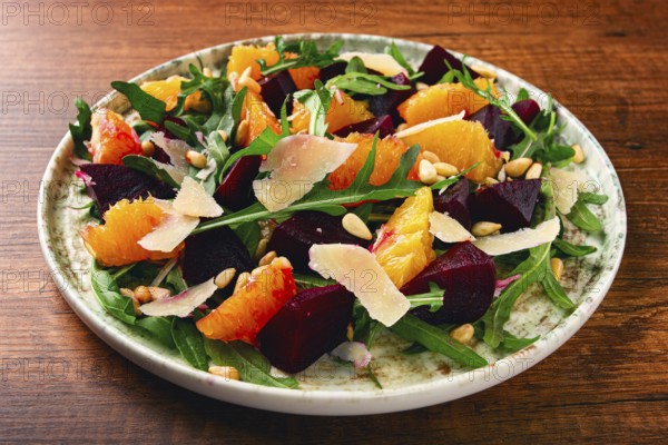 A bowl of salad contains beetroot, orange slices, pine nuts, and leaves. It is placed on a wooden table. The meal is healthy and looks colorful