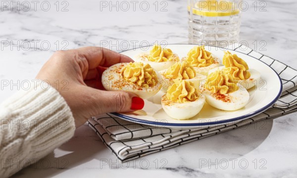 Stuffed eggs with paprika, on a plate, a woman's hand reaches for it