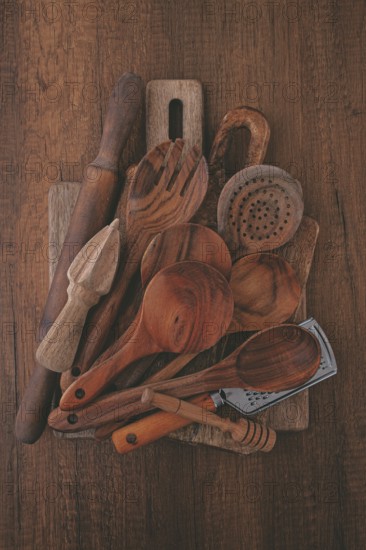 Various wooden kitchen utensils, including spoons, a rolling pin, and a strainer, are artistically placed on a rustic wooden surface, showcasing their natural beauty and craftsmanship