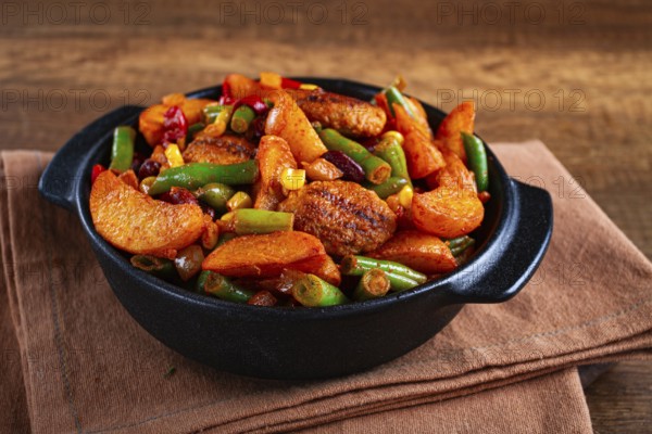 Steakhouse pfanne, fried potato slices, with meatballs, and vegetable mixture, on a black plate