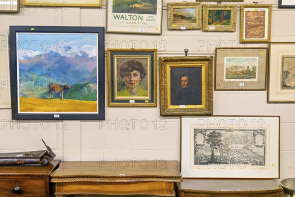 Various lots of pictures and paintings hanging on wall at auction house, UK