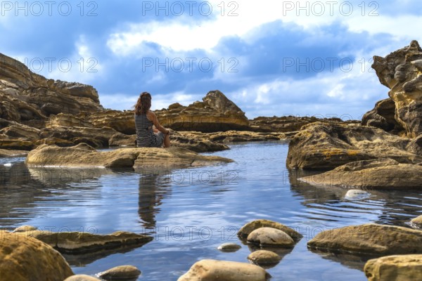 Woman sitting alone on a rock surrounded by shallow calm water and eroded rock formations, reflecting solitude and peace in a beautiful outdoor landscape