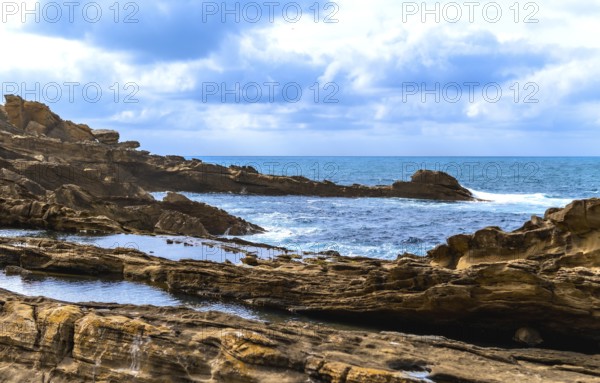 Ocean waves crashing on a rugged rocky coastline with tide pools reflecting the cloudy sky, capturing the raw beauty and power of nature and coastal erosion
