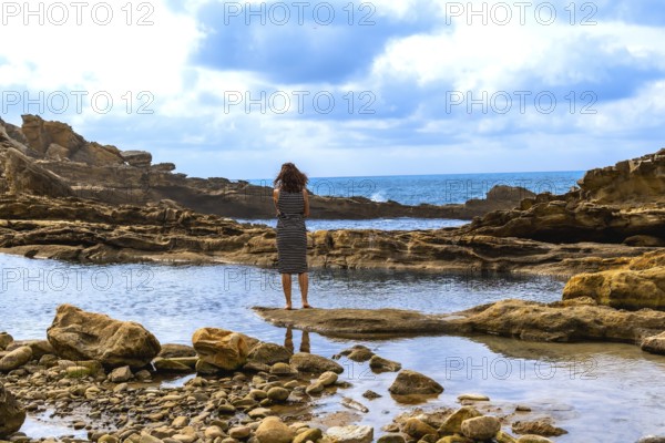 Woman standing on a natural rock formation, looking out at the rugged jaizkibel coast and atlantic ocean, finding solitude and contemplation by the sea