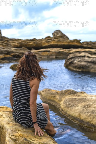 Woman sitting on coastal rock formations, enjoying the calm water and rugged landscape of jaizkibel, experiencing tranquility and connection with nature