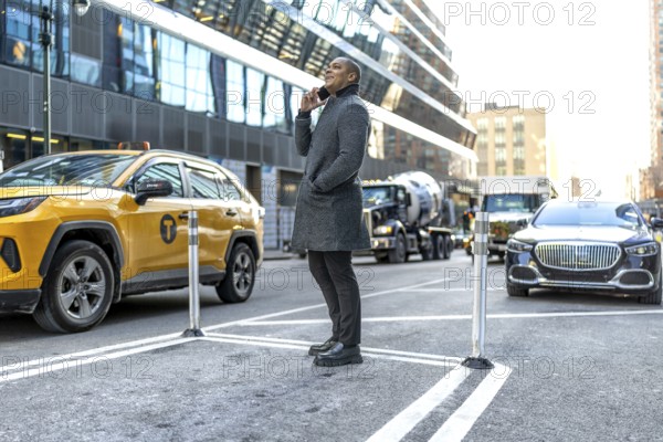 Businessman standing on a bustling manhattan street, having an important conversation on his mobile phone while surrounded by city traffic and modern architecture
