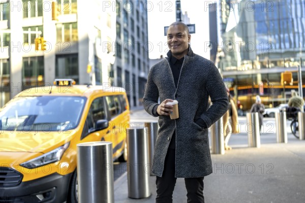 Businessman standing on a new york city street with a coffee cup, a yellow taxi passing in the background, representing daily urban life and a busy professional lifestyle