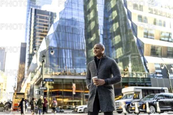 Happy business professional standing on a busy manhattan street, holding a takeaway coffee cup, looking forward with strength and confidence, surrounded by modern skyscrapers and urban activity