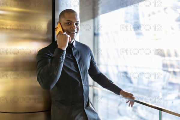Confident businessman connecting with clients on a mobile phone, discussing future projects and business ventures while leaning against a wall in a modern new york city building