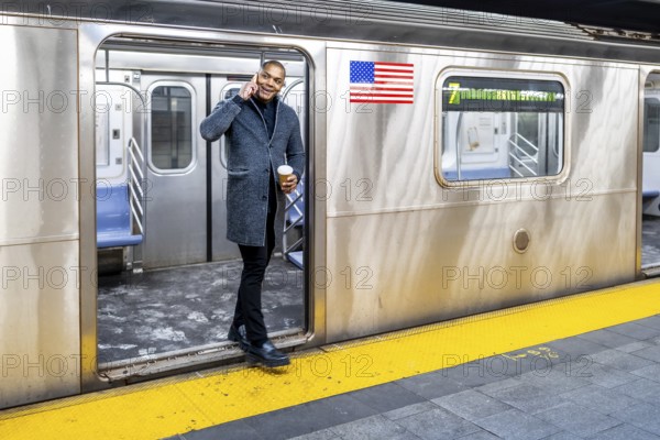 Man in smart casual attire holding coffee and talking on his mobile phone as he steps off a crowded manhattan subway onto the platform during a busy commute