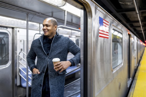 Young businessman boarding a new york city subway, smiling with a takeaway coffee as he steps onto the train during his morning commute through the busy station