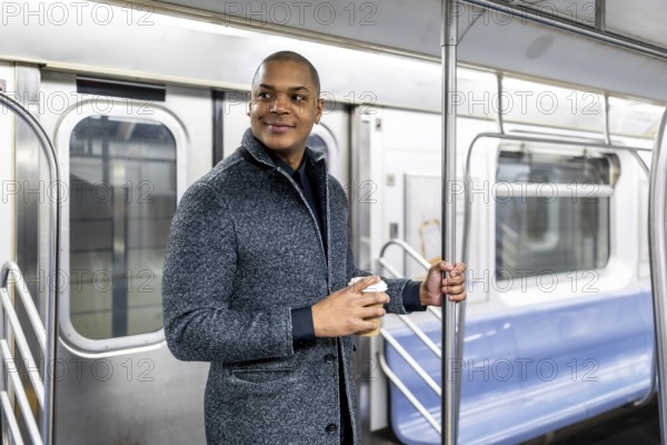 Young businessman traveling by public transport in manhattan, holding a coffee cup and looking confidently towards his destination while riding the metro