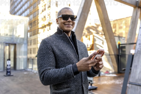 Businessman in modern sunglasses looking at new horizons while standing in a busy urban setting, using a mobile phone to connect and manage work on the go in new york city
