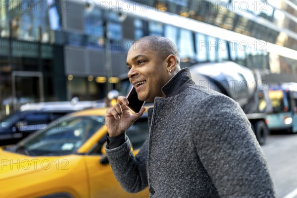 Young black businessman is walking on a city street in manhattan, new york, laughing while having a phone conversation, showing a modern urban lifestyle, communication, and connectivity