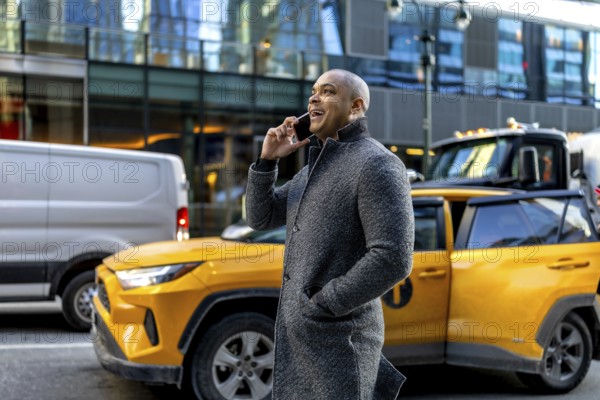 Happy professional businessman talking on a mobile phone, standing on a bustling urban street with a yellow taxi and buildings in the background, representing communication, success, and city life