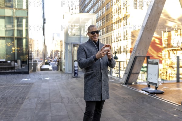 Happy professional man walking and using a smartphone in a bustling manhattan street environment, showcasing urban connectivity, modern lifestyle, and business on the go