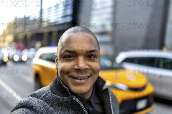Smiling african american businessman taking a selfie on a vibrant city street, showcasing a professional and approachable demeanor amidst the bustling new york city urban background