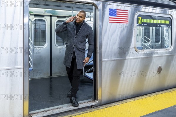 Professional man talking on a mobile phone exiting a subway train at a station platform in new york city, demonstrating urban connectivity and busy city commuting