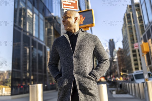 Young man smiling confidently as he walks through manhattan's financial district in smart casual attire, sunny blue sky and modern skyscrapers framing his commute and success