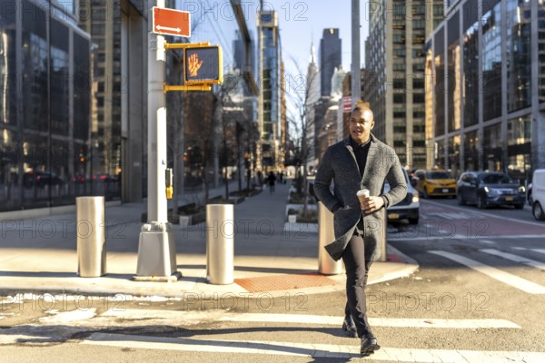 Young businessman walking confidently across a crosswalk in manhattan with a coffee cup, showcasing urban lifestyle and dynamic city energy against a backdrop of modern skyscrapers