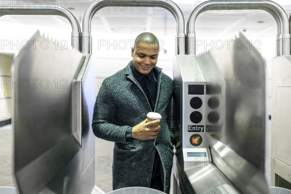 Young professional passing a manhattan subway turnstile with a takeaway coffee, entering the metro for his morning commute amid bustling urban transit and rush hour energy