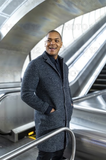 Young black businessman smiling and looking away while riding an escalator in a modern subway station, representing urban lifestyle, success, and daily commute in new york city