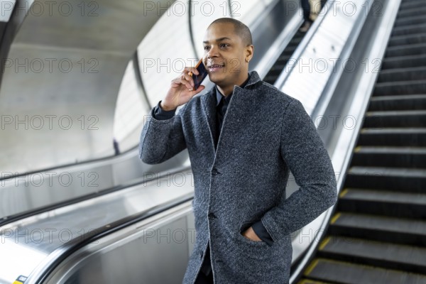 Young businessman talking on his smartphone while traveling on an escalator in a manhattan subway station, navigating urban commuting and connecting during his busy day