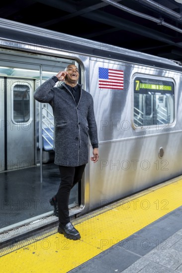 Happy professional man smiling and talking on smartphone while stepping onto a manhattan subway train, commuting through a bustling urban station for work and travel