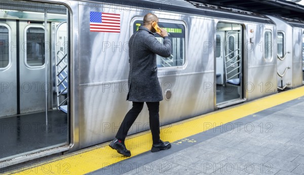 Man walking on the subway platform, talking on a mobile phone while waiting to board a train, symbolizing urban connectivity, daily commute, and busy city life in manhattan