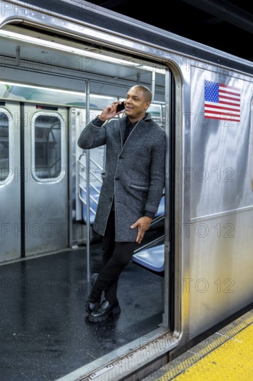 Young man standing confidently in a subway car doorway, talking on his smartphone, representing urban connectivity, communication, and commuting in the city